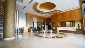 A modern hotel lobby with a reception desk, seating area, and a large column. - Grand Estancia (Salem)