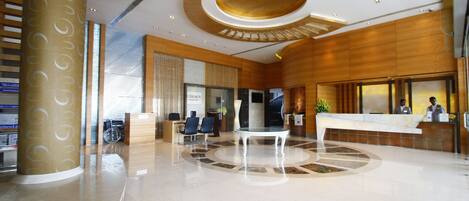 A modern hotel lobby with a reception desk, seating area, and a large column.