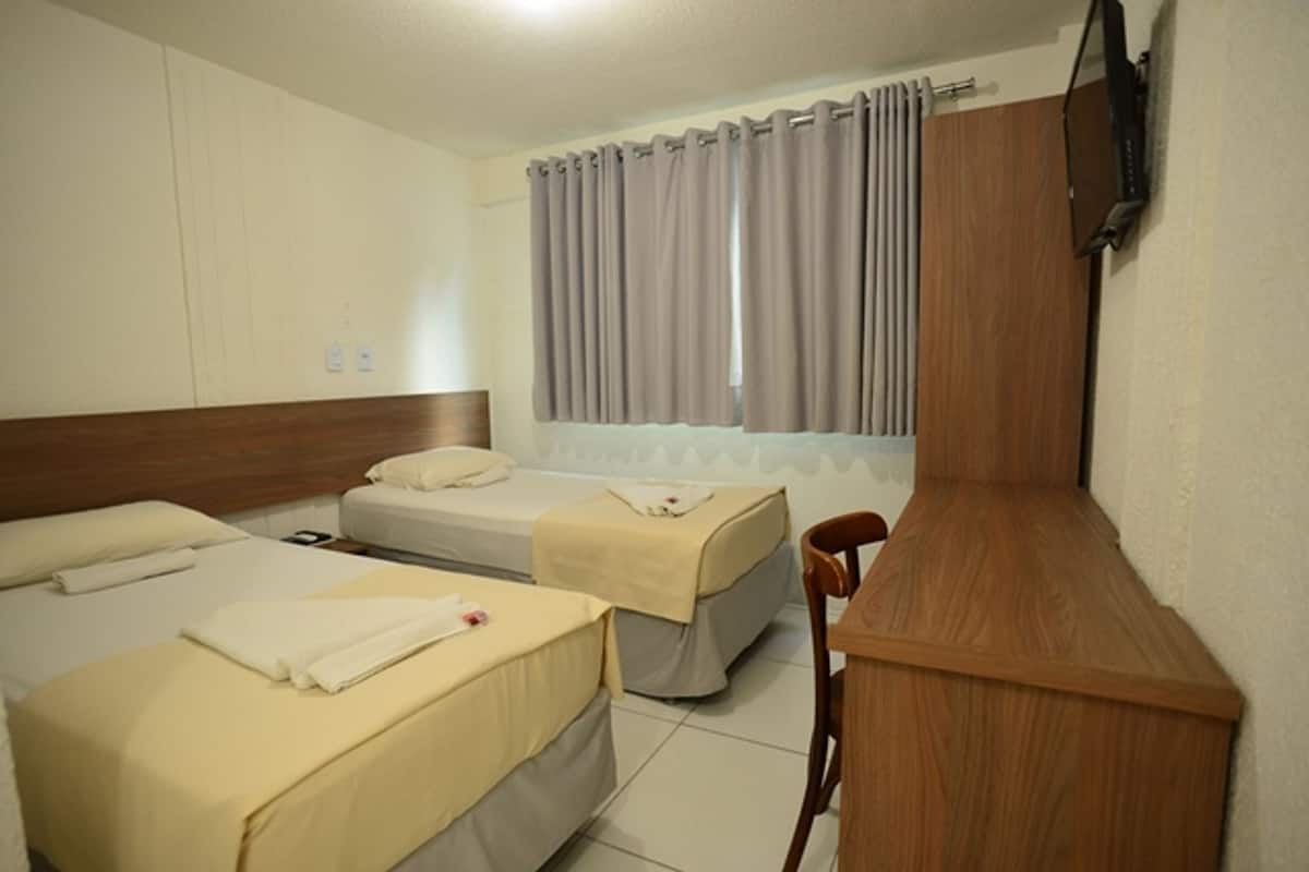 Una habitación de hotel con dos camas, un escritorio de madera y un televisor montado en la pared.