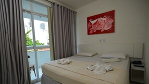 A hotel room with a bed, a nightstand, a red abstract painting, and a view of greenery through the window. - Alpha Praia Hotel (Fortaleza)
