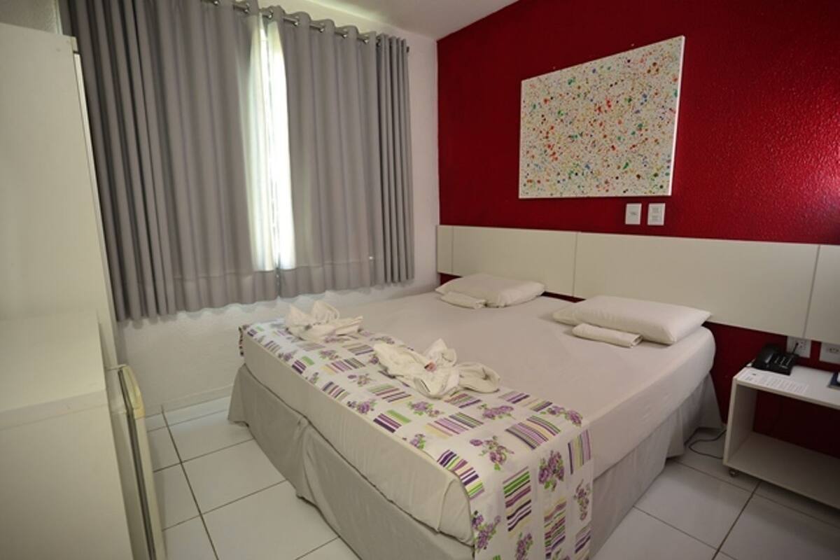Una habitación de hotel con una cama grande, un escritorio, un teléfono y un cuadro en la pared.