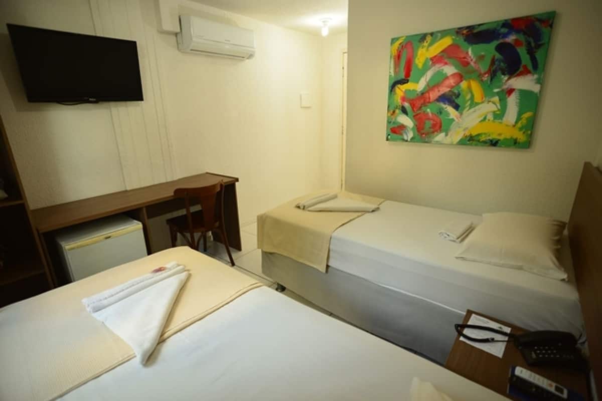 Habitación de hotel con dos camas, un escritorio, una silla, un televisor y un cuadro de colores en la pared.