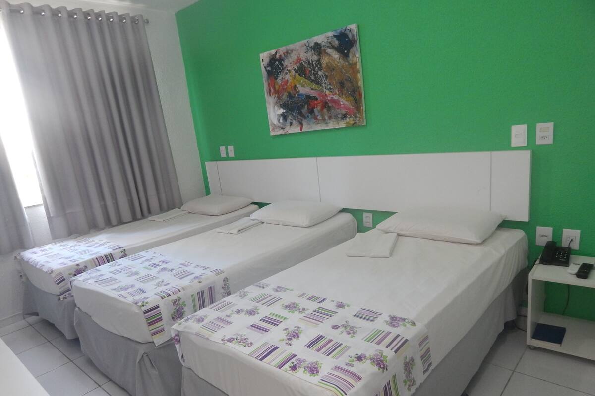 Habitación de hotel con dos camas individuales, una pared verde, un cuadro y una mesita de noche pequeña con un teléfono.
