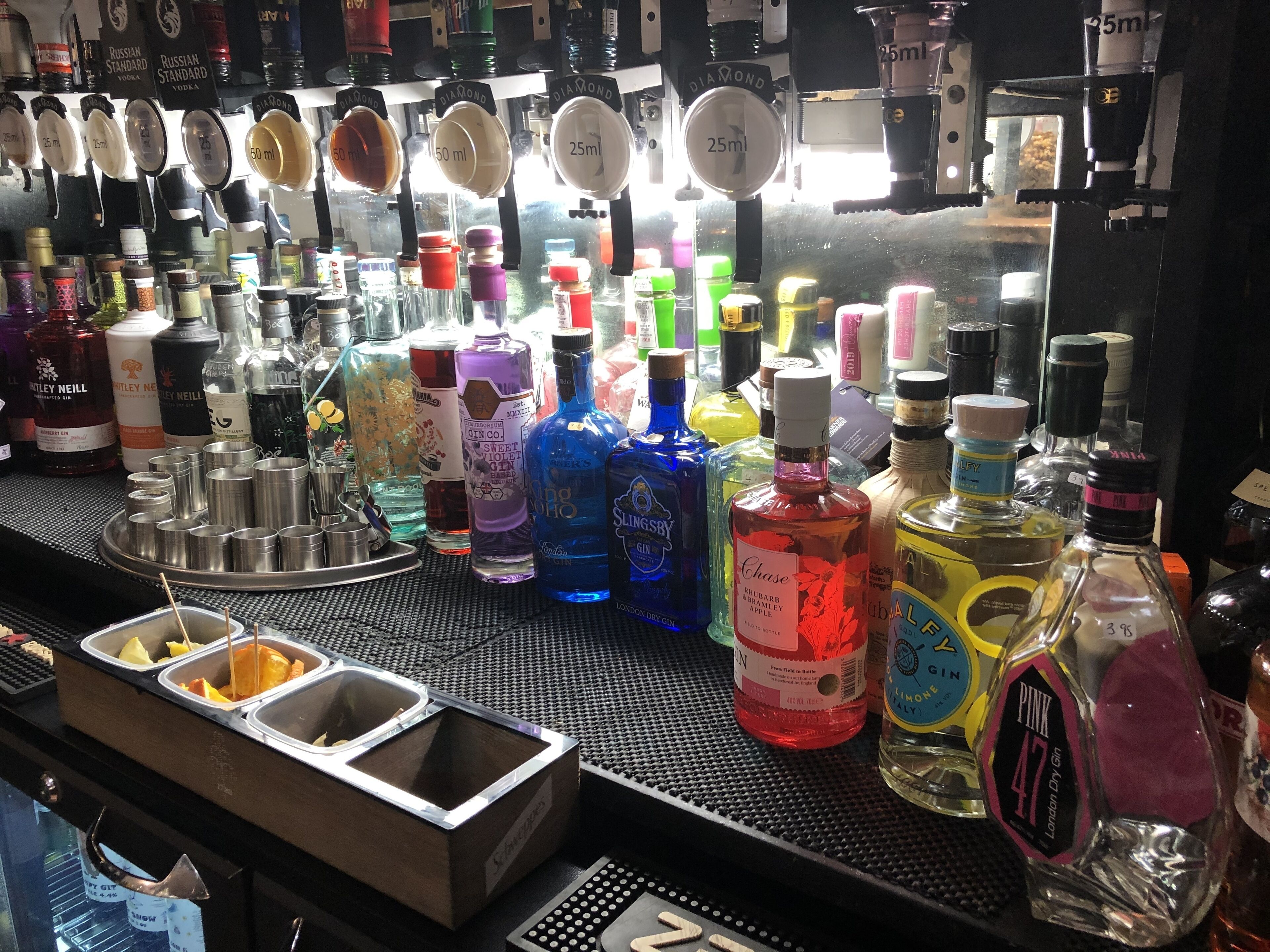 A bar with various bottles of alcohol, including gin and vodka, and a tray with orange slices.