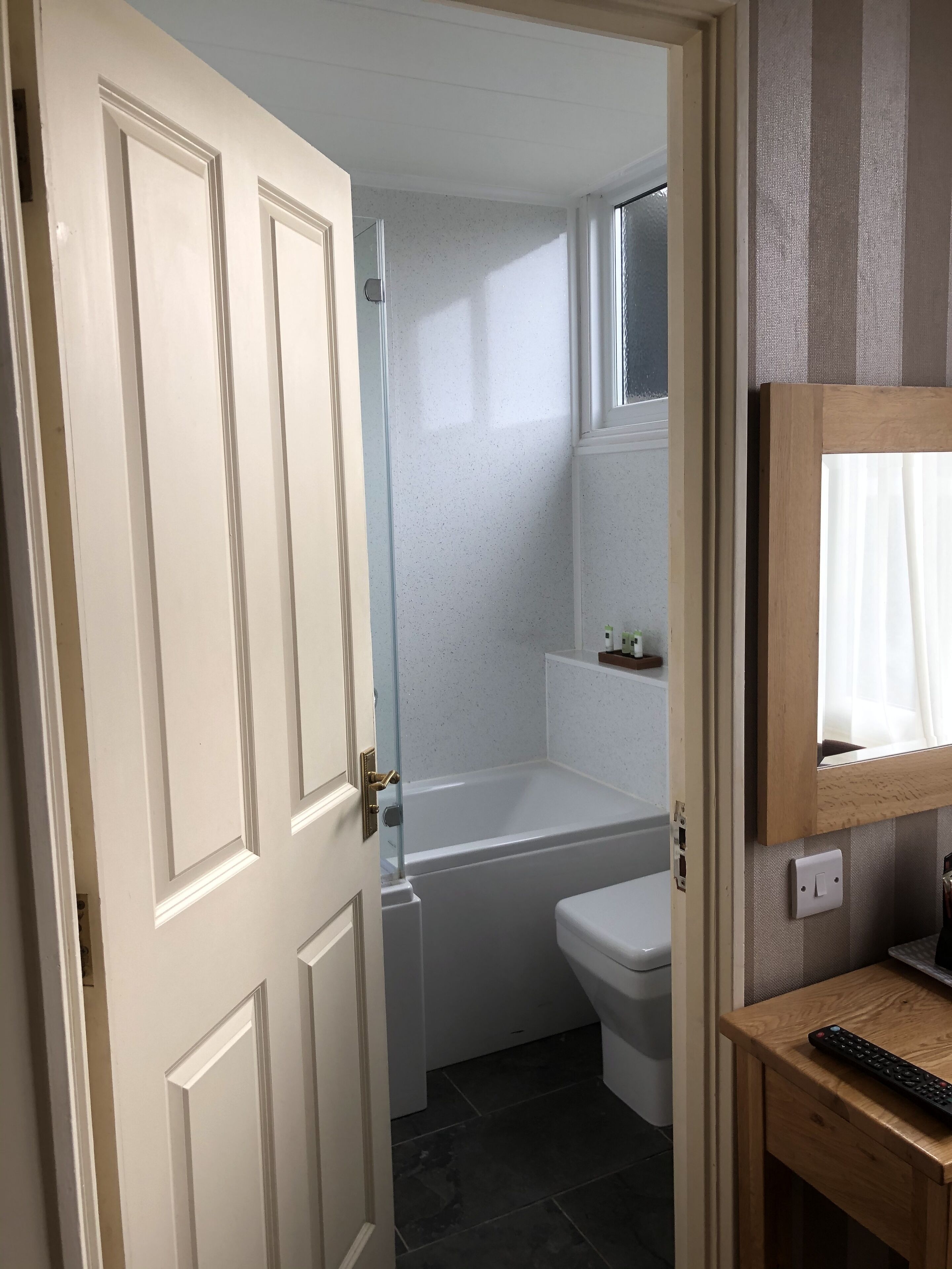 A bathroom with a bathtub, toilet, and a small window.