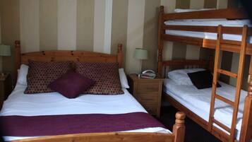 A room with a single bed, a nightstand, a bedside table, and a bunk bed.