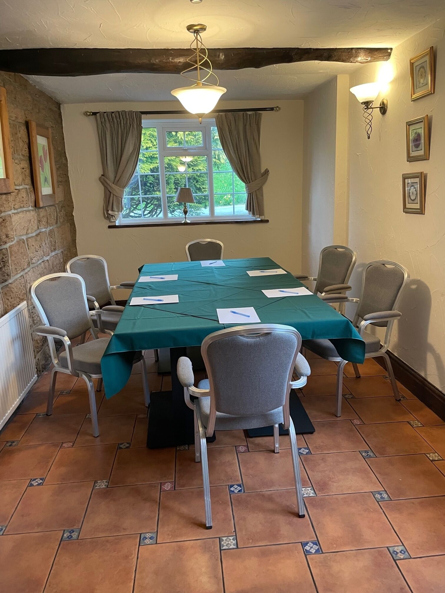A conference room with a long table, six chairs, a green tablecloth, and a window with curtains.