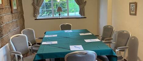 A conference room with a long table, six chairs, a green tablecloth, and a window with curtains.