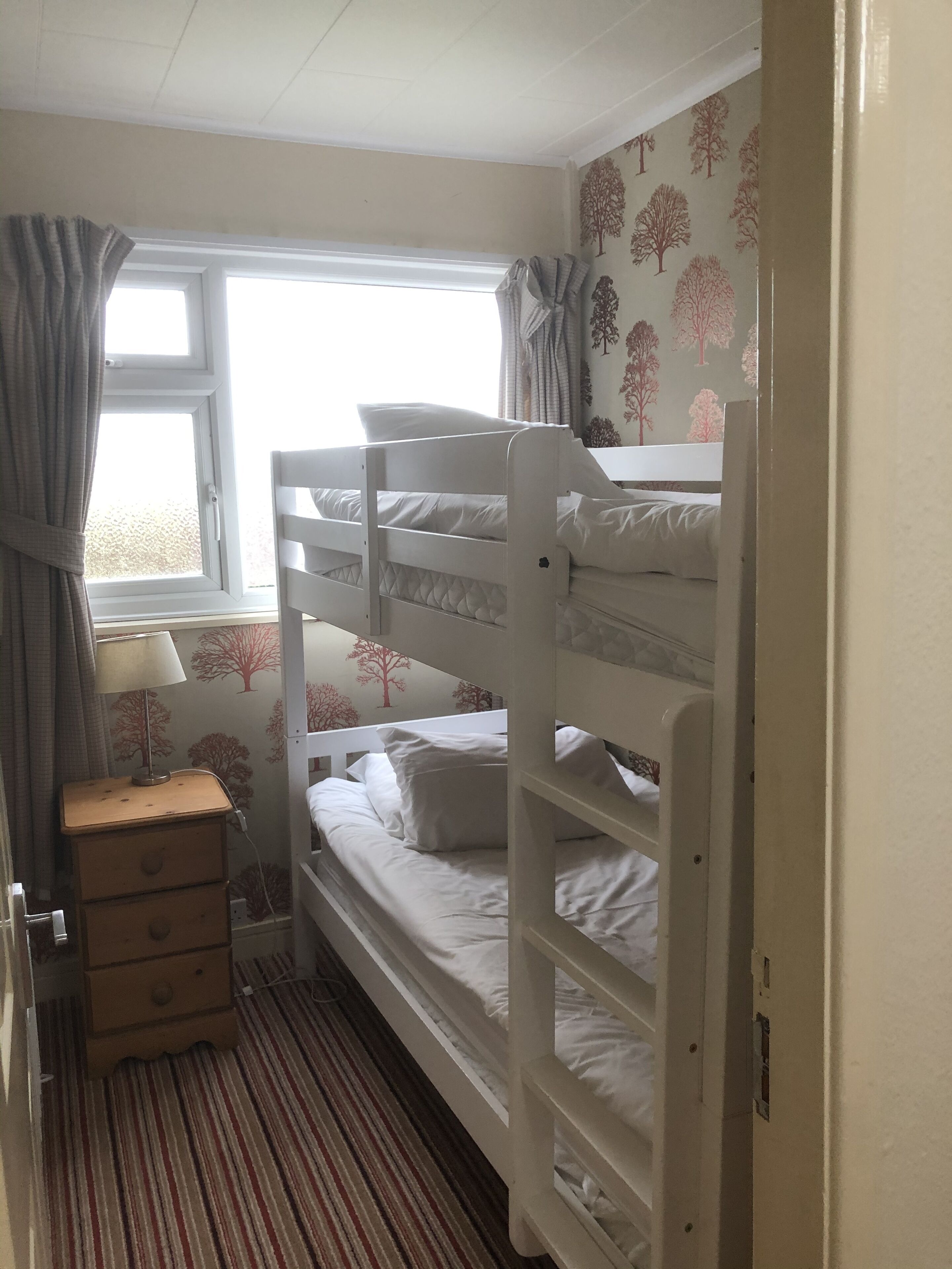A bunk bed room with a window, a bedside table, and a dresser.