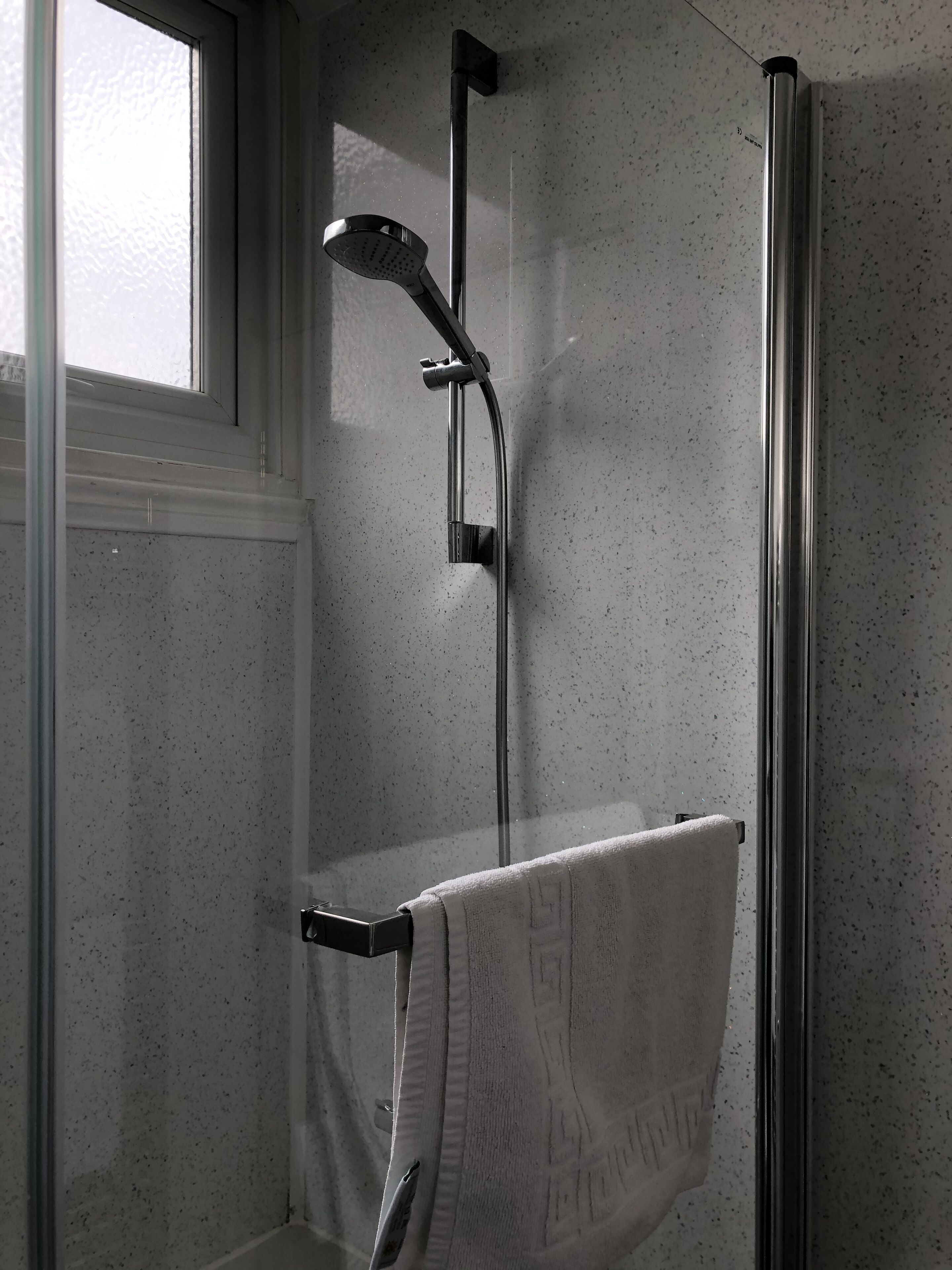 A bathroom with a glass-enclosed shower, a white towel hanging on a rack, and a window providing natural light.