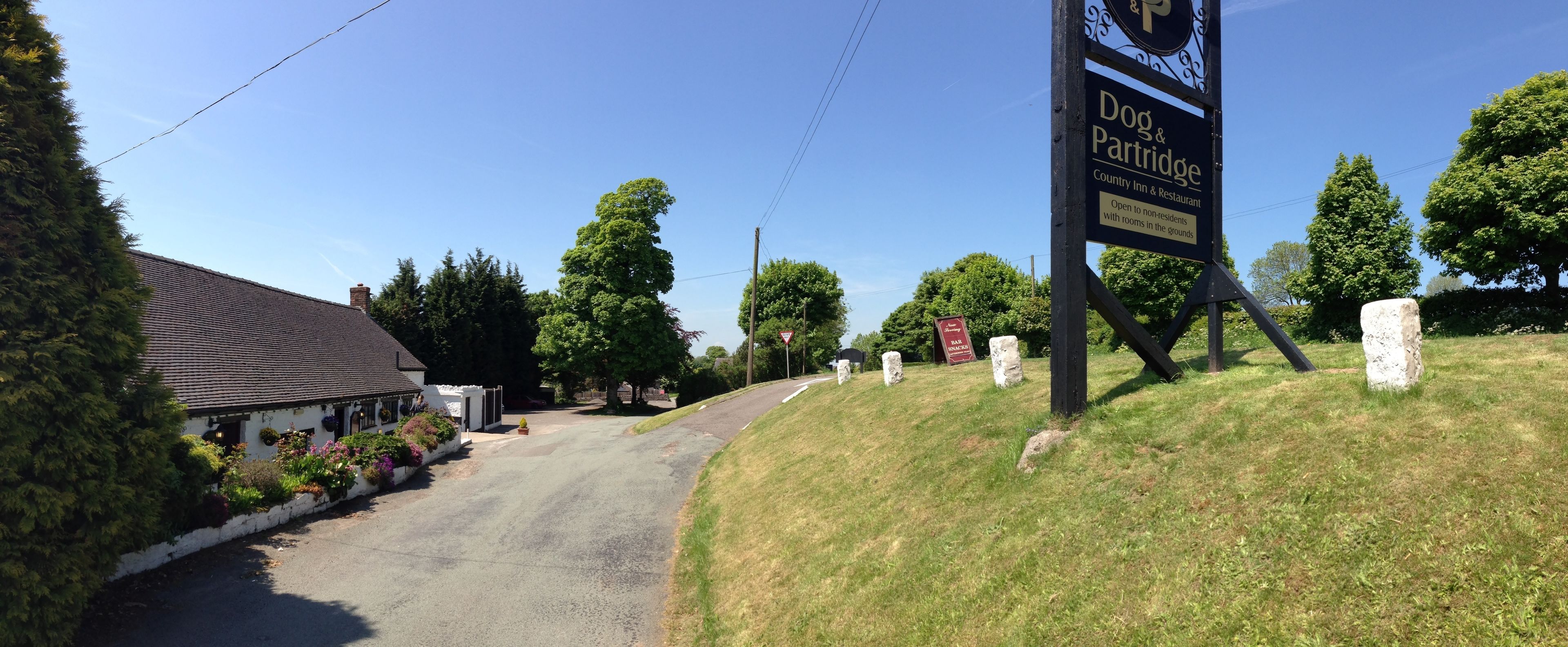 Eine Landstraße führt zum Dog & Partridge Country Inn & Restaurant, mit einem Schild und Steinmarkierungen.