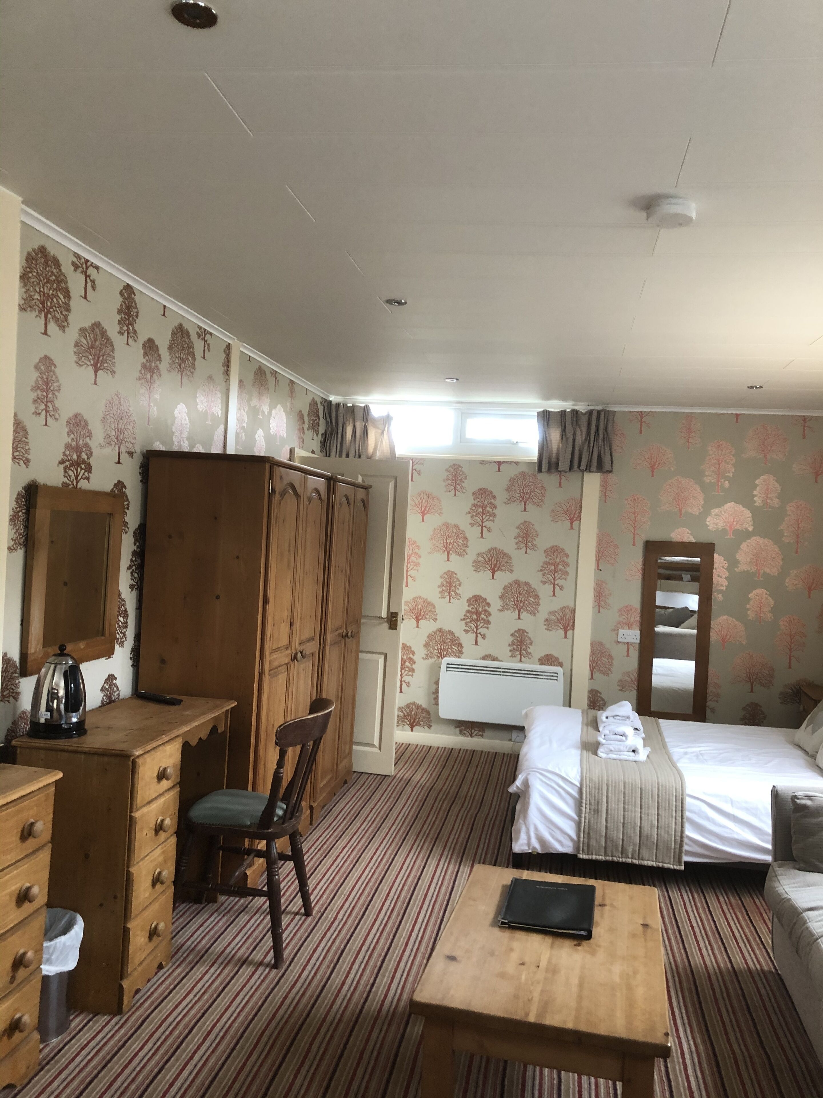 A room with a bed, a wooden desk, a chair, a small table, and a wardrobe.