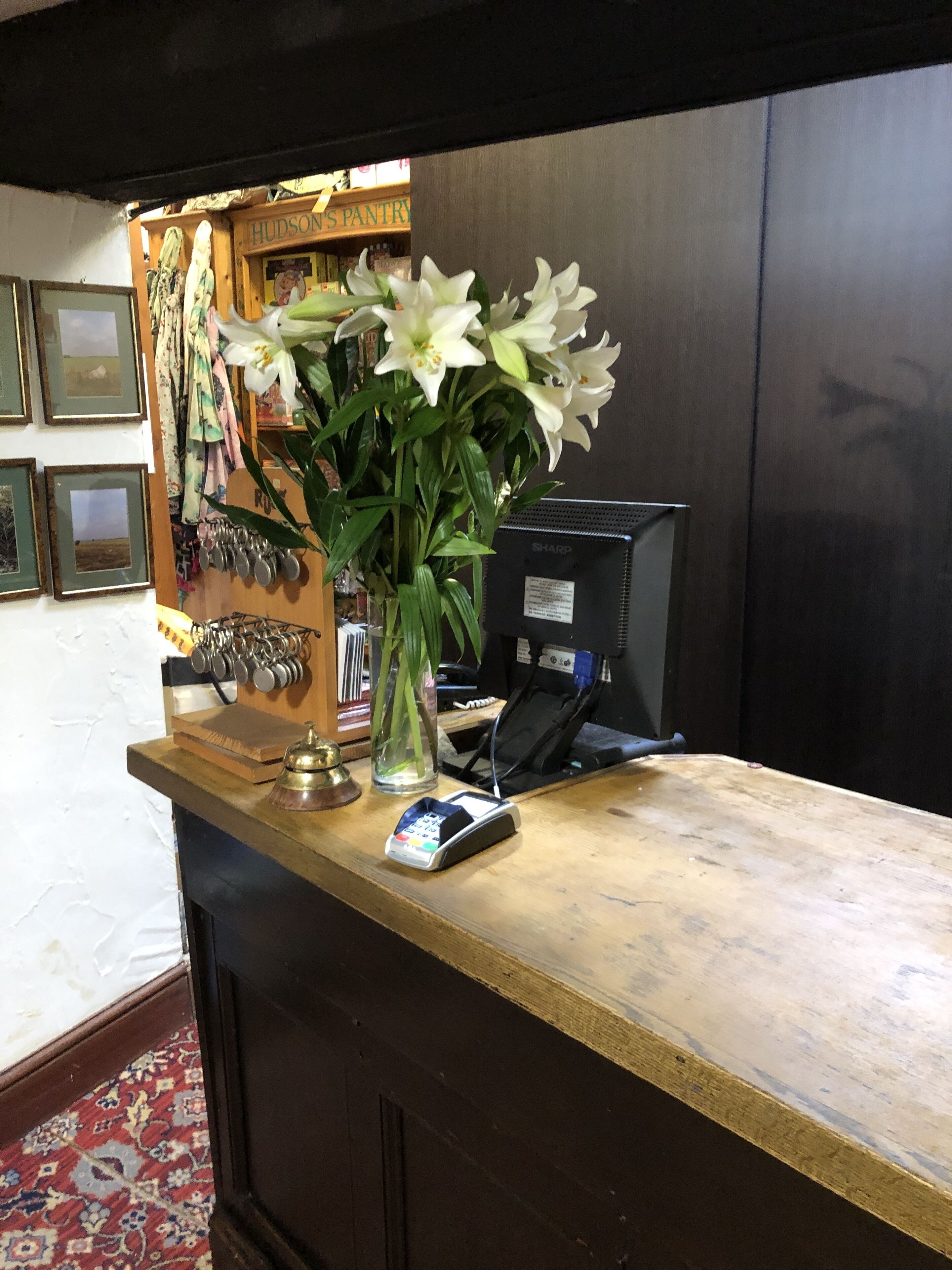A reception desk with a vase of white flowers, a cash register, and a computer monitor.