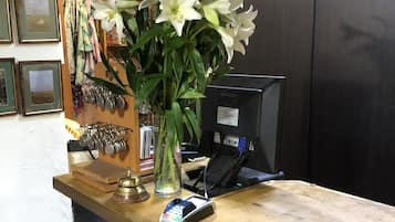 A reception desk with a vase of white flowers, a cash register, and a computer monitor.