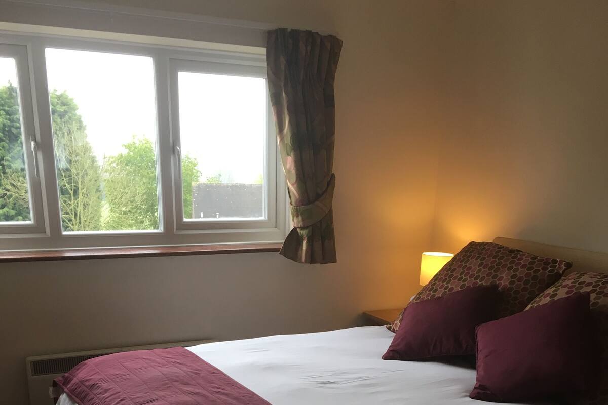 A hotel room with a bed, a window with curtains, a night lamp, and a radiator.
