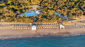 En vy från ovan av ett semesterområde med en swimmingpool, parasoller och en strand.