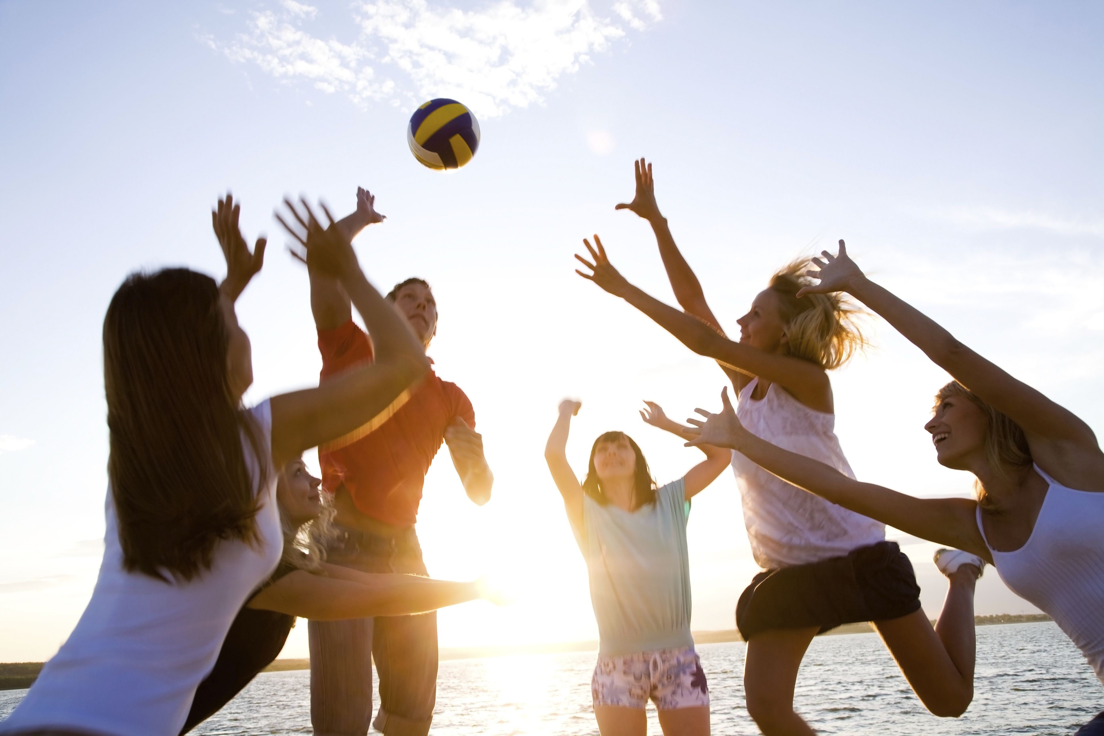 Een groep mensen speelt volleybal bij zonsondergang aan het water.