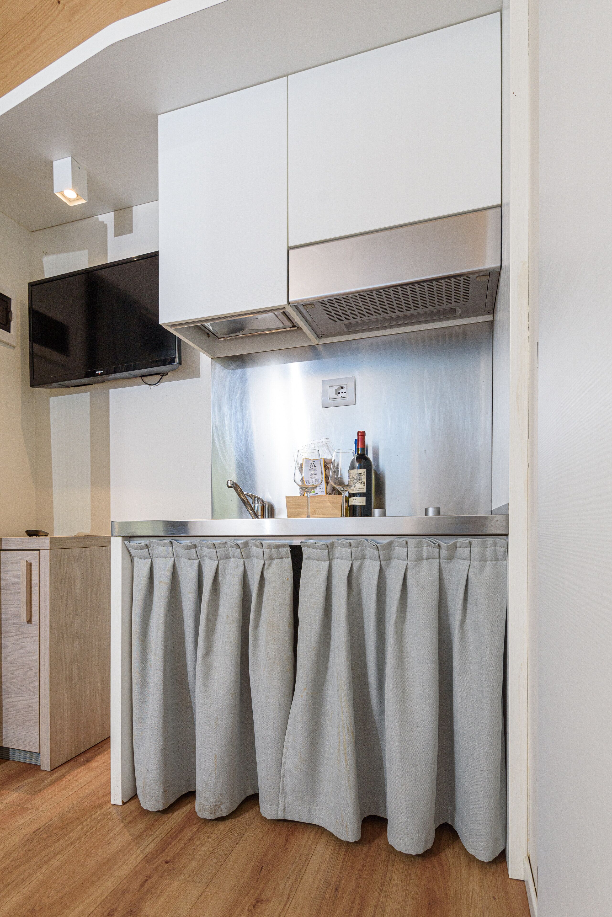 A compact kitchen with white cabinets, a stainless steel countertop, and a grey curtain.