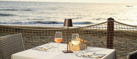 A table set for two with a view of the ocean, a lamp, and a glass of wine.