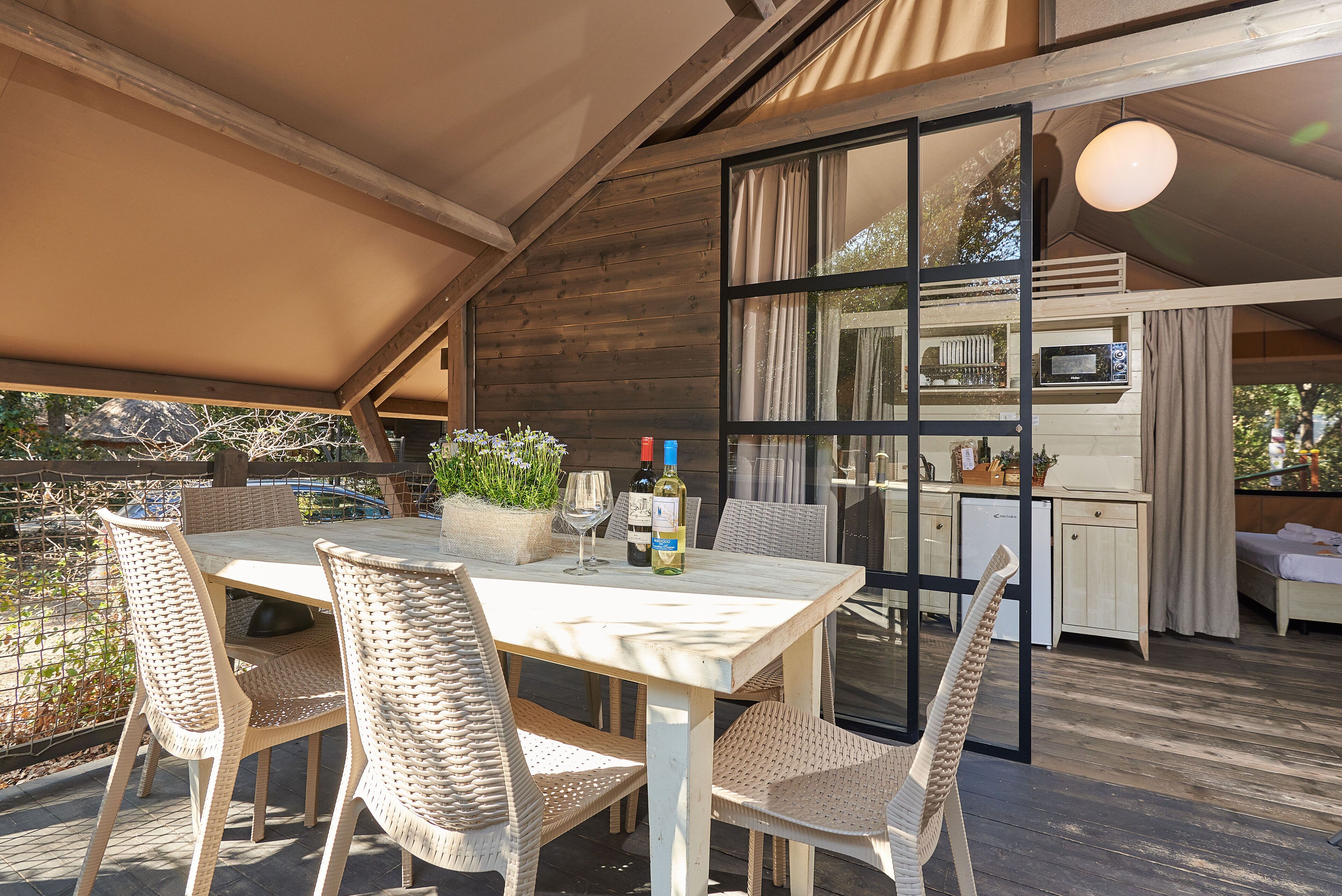 An outdoor dining area with wicker chairs and a table, a kitchen with a microwave, and a large window.