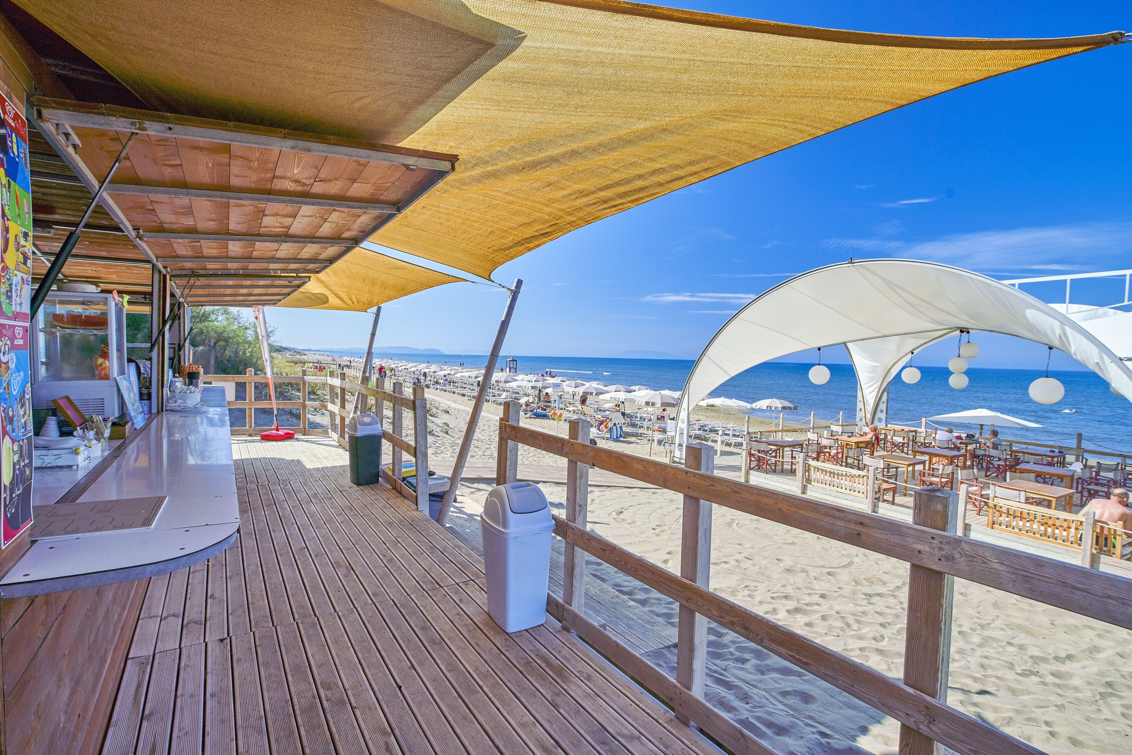 A wooden deck with a beach view, a white canopy, and a trash bin.