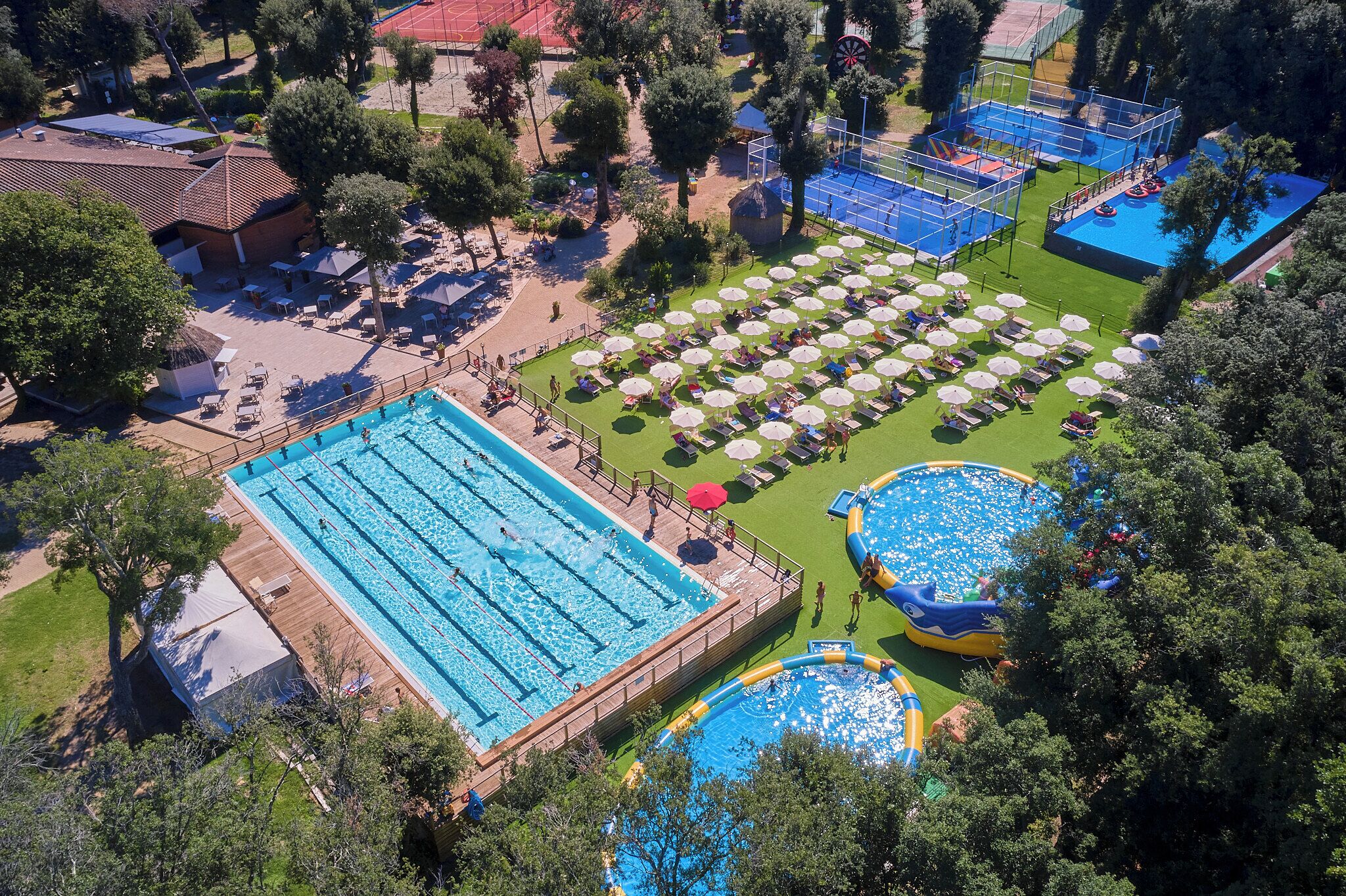 Una amplia piscina exterior con varias pistas, rodeada de tumbonas y sombrillas.