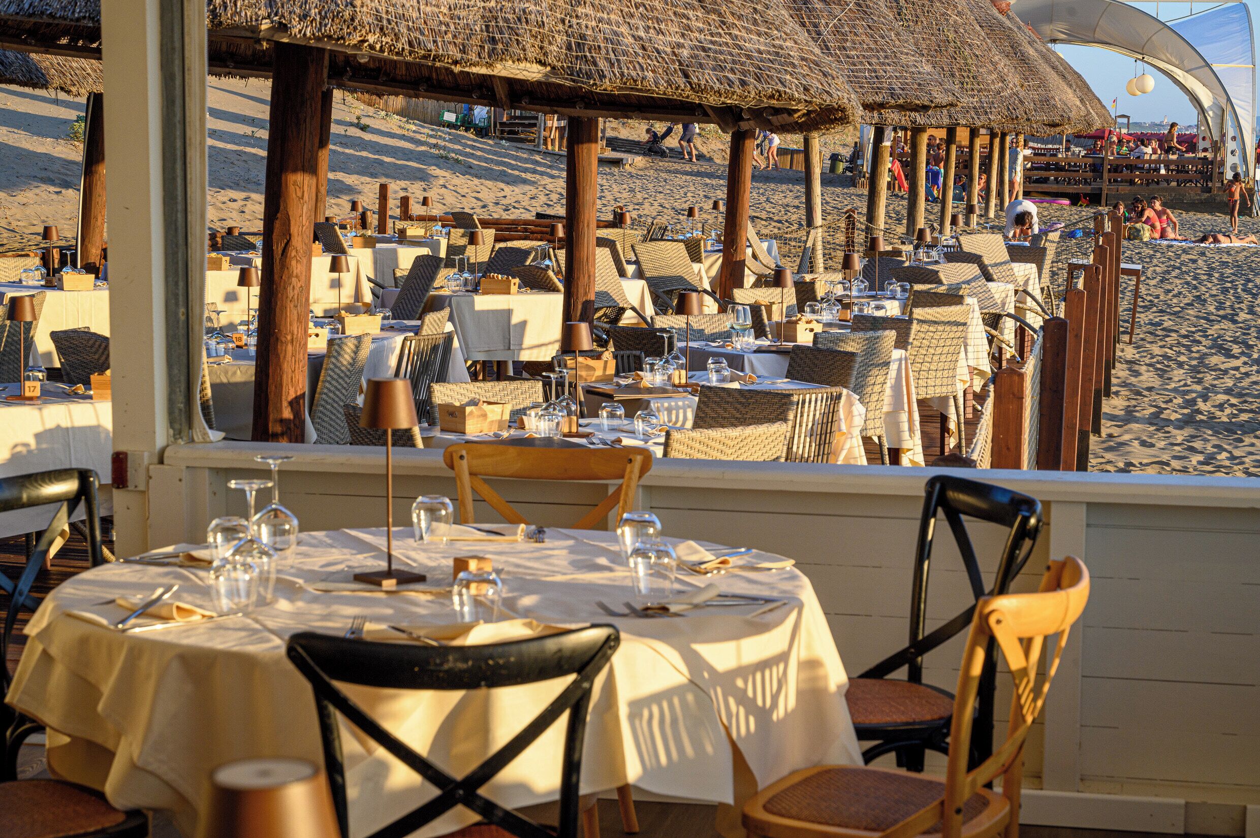 Restaurante al aire libre con mesas dispuestas para comer, con vistas a una playa.