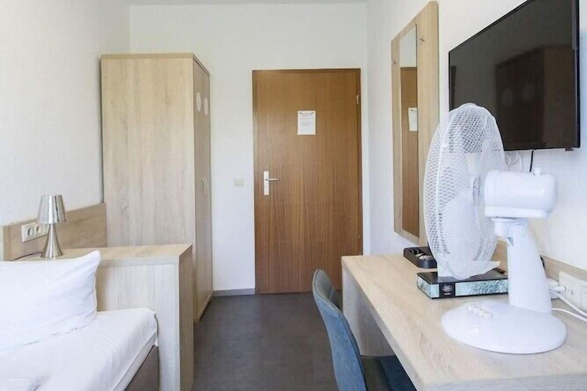 A hotel room with a bed, a desk with a fan, a television, and a wardrobe.