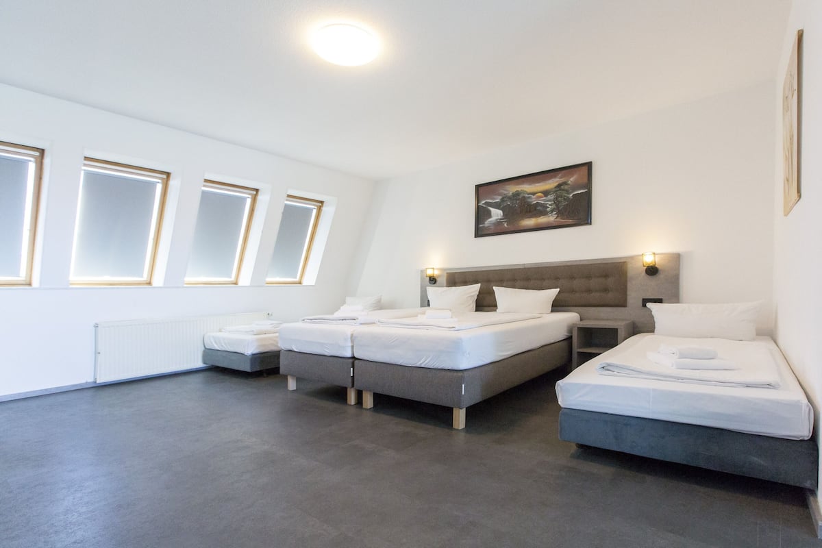 A modern hotel room with two beds, a large window, and a painting on the wall.