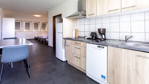 A modern kitchen with a dishwasher, a coffee maker, and a sink. There is a dining area with a table and chairs. - Pension Odin (Berlin)