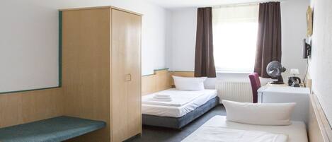 A hotel room with a single bed, a desk, a chair, a wardrobe, and a window with curtains.