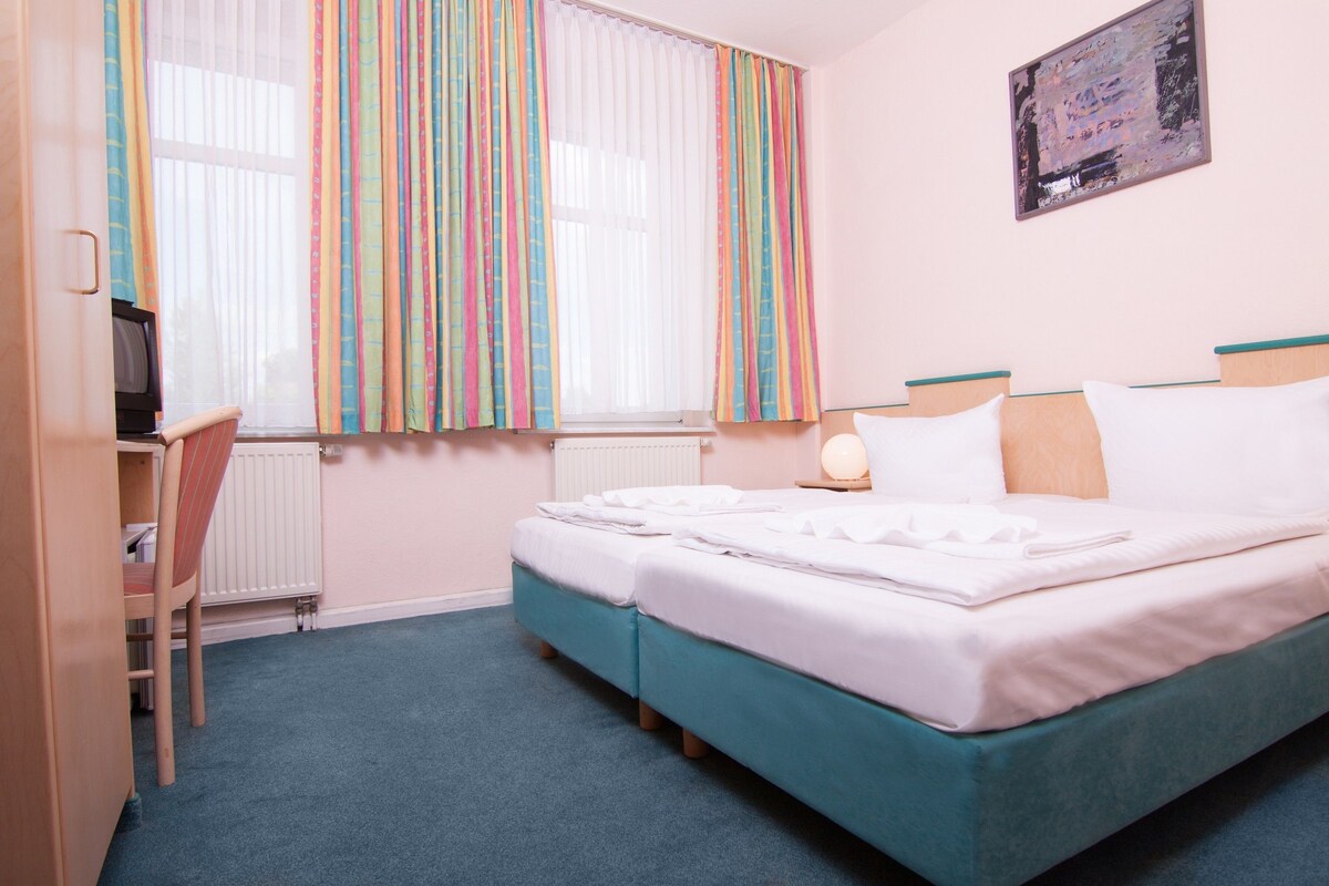 A hotel room with a bed, a desk, a chair, and a window with curtains.