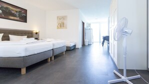 A hotel room with a bed, two bedside tables, a standing fan, and a hallway leading to a bathroom. - Pension Odin (Berlin)