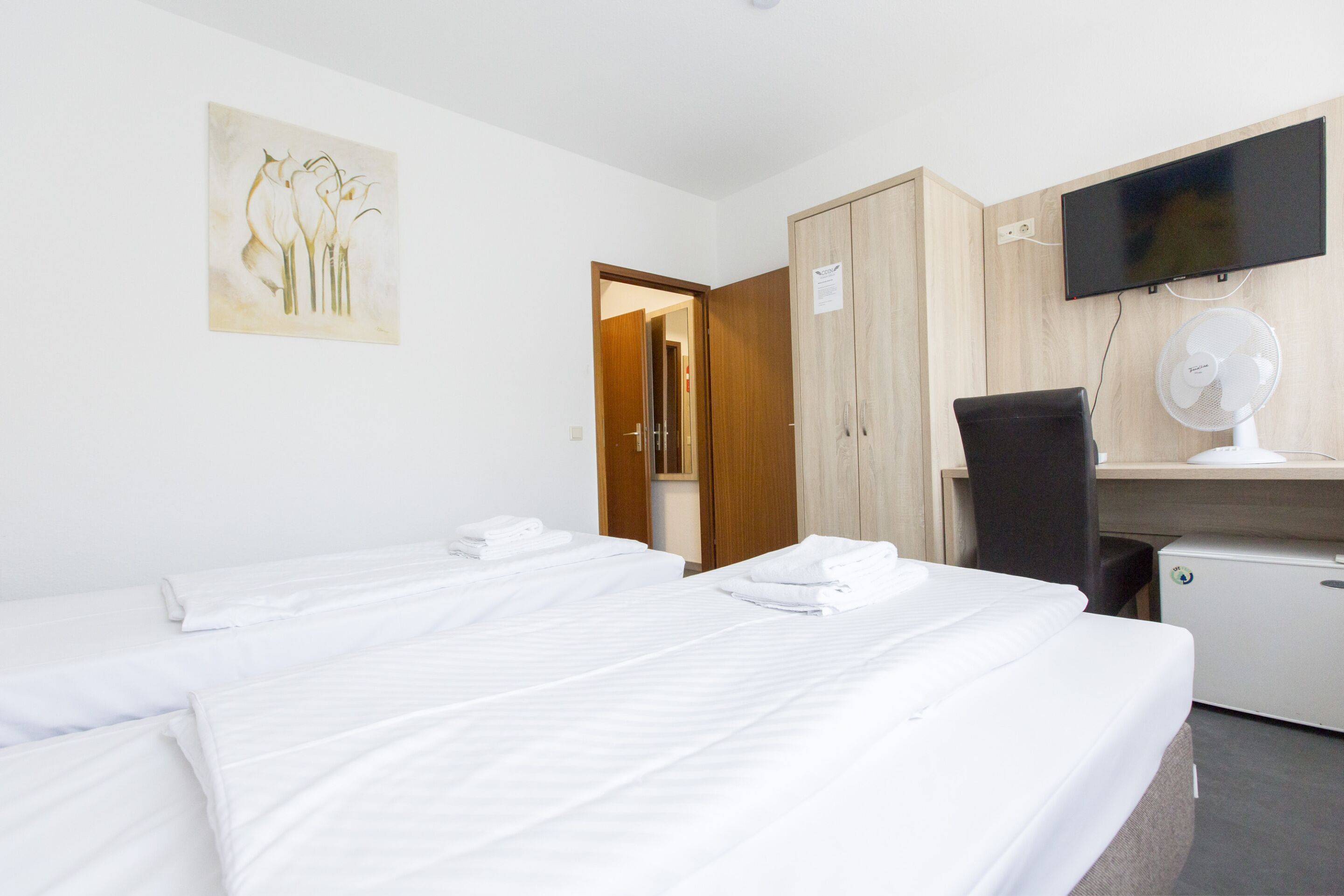 Een hotelkamer met twee bedden, een bureau met een computer, een televisie en een ventilator.