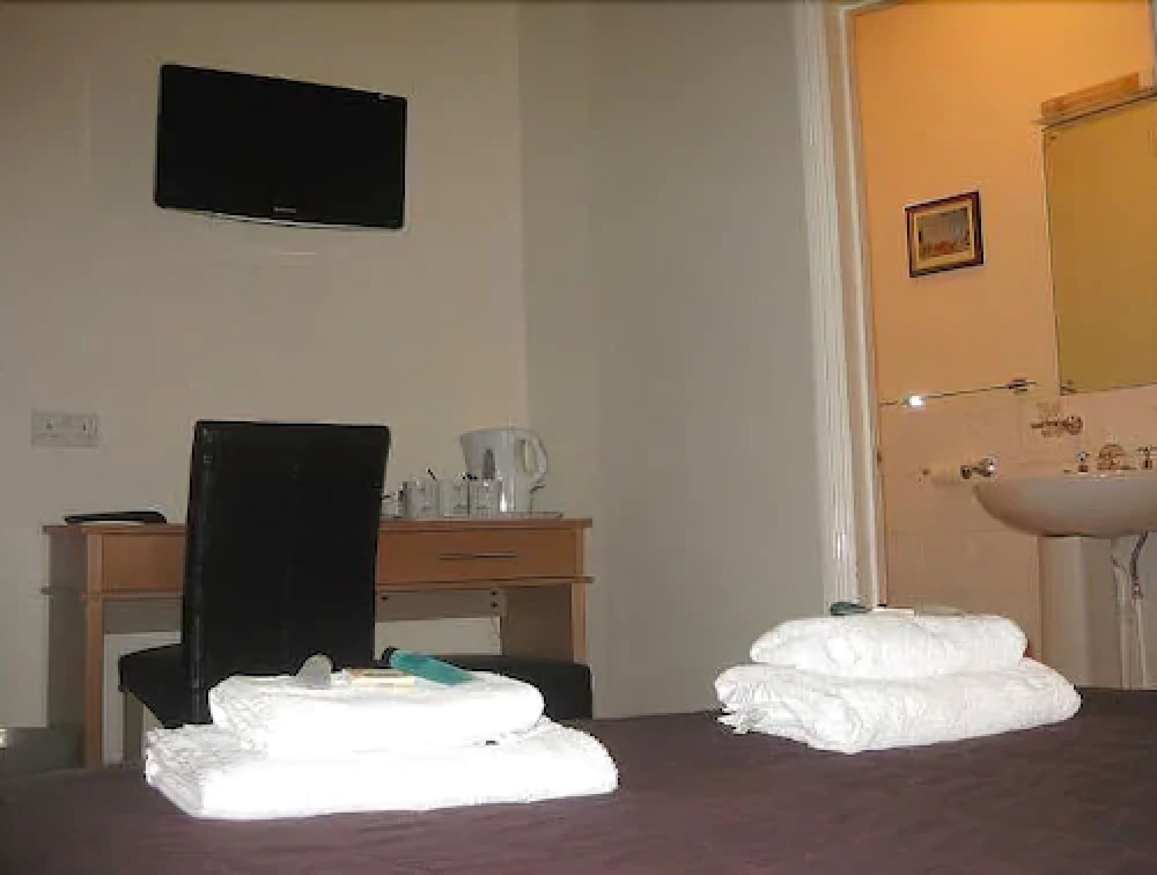 Een hotelkamer met een bed, een bureau met stoel, een aan de muur bevestigde televisie en een badkamer met wastafel en spiegel.