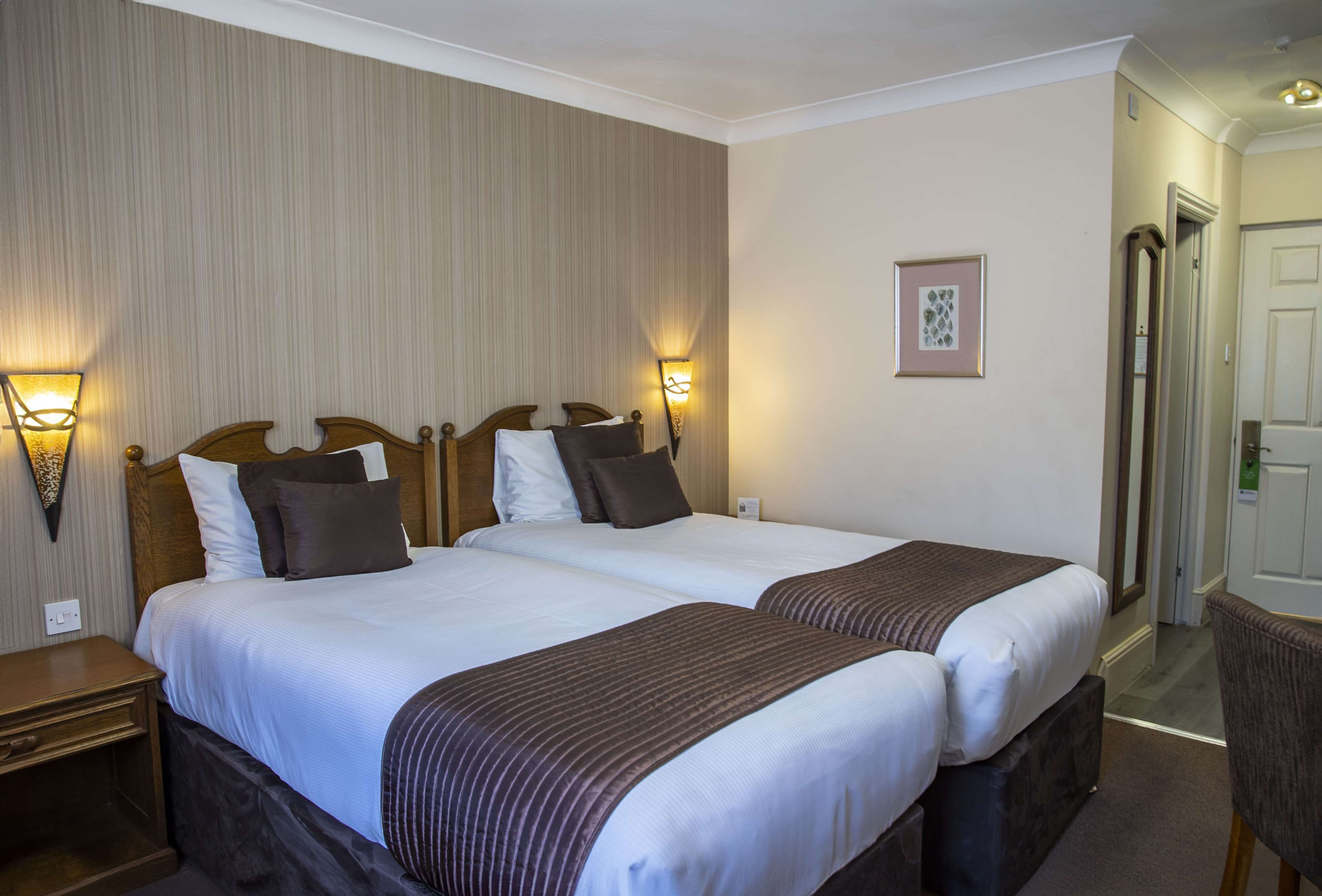 A hotel room with two beds, nightstands, wall-mounted lamps, and a framed picture on the wall.