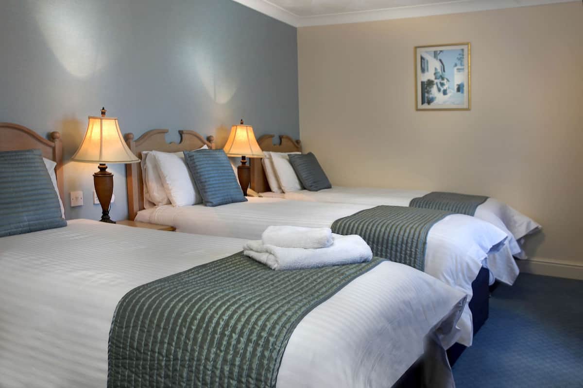 A hotel room with two beds, each with a lamp, pillows, and a blanket.
