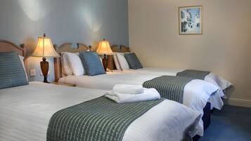 A hotel room with two beds, each with a lamp, pillows, and a blanket.