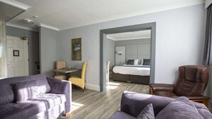 A modern hotel room with a grey sofa, a brown leather chair, and a bed with a white headboard. - Best Western Manor Hotel (Gravesend)