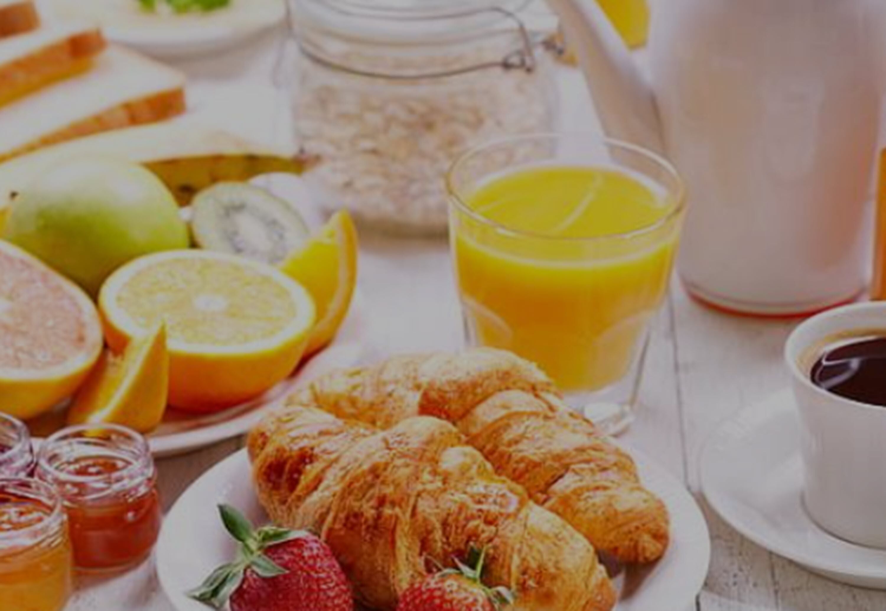 Ein Frühstücksbrett mit Croissants, Erdbeeren, Orangenscheiben, Kiwis und einem Glas Orangensaft.