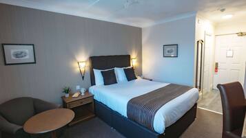 A hotel room with a large bed, bedside tables, a small round table, two chairs, and framed pictures on the walls.