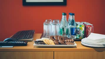 Un escritorio con un teclado, un plato de galletas, botellas de agua y latas de refresco.