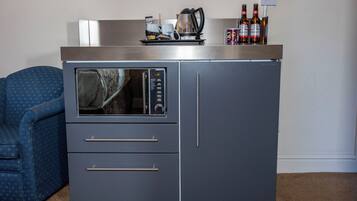 A compact kitchenette with a microwave, two drawers, and a countertop with a kettle, coffee maker, and bottles.