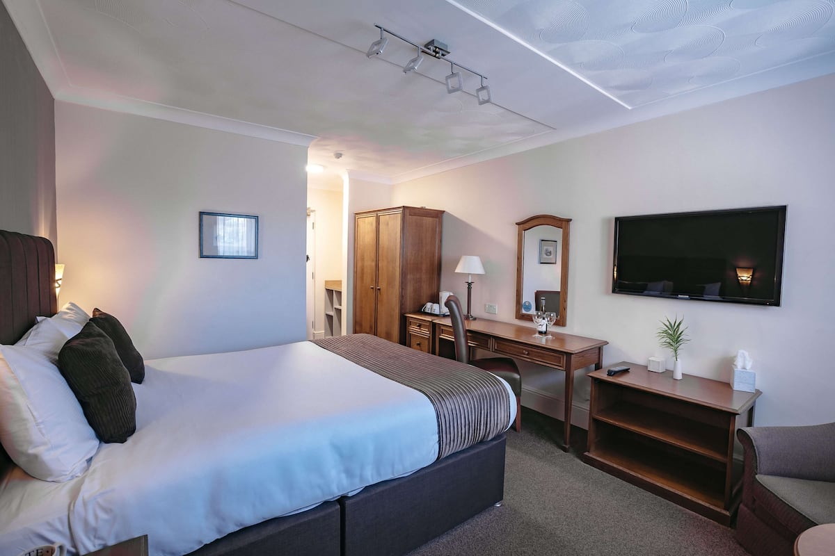 A hotel room with a bed, desk, wardrobe, and a TV on the wall.