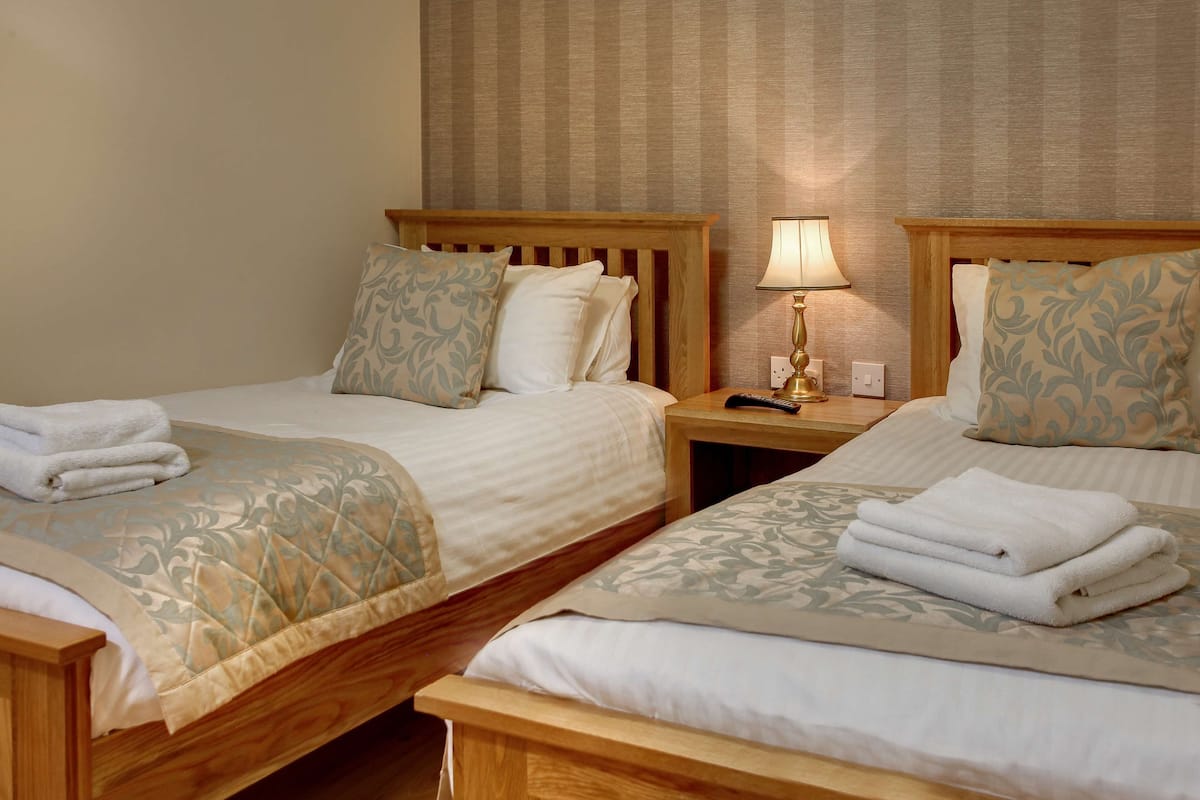 Two wooden beds with matching headboards and footboards, each with a bedside table and lamp.