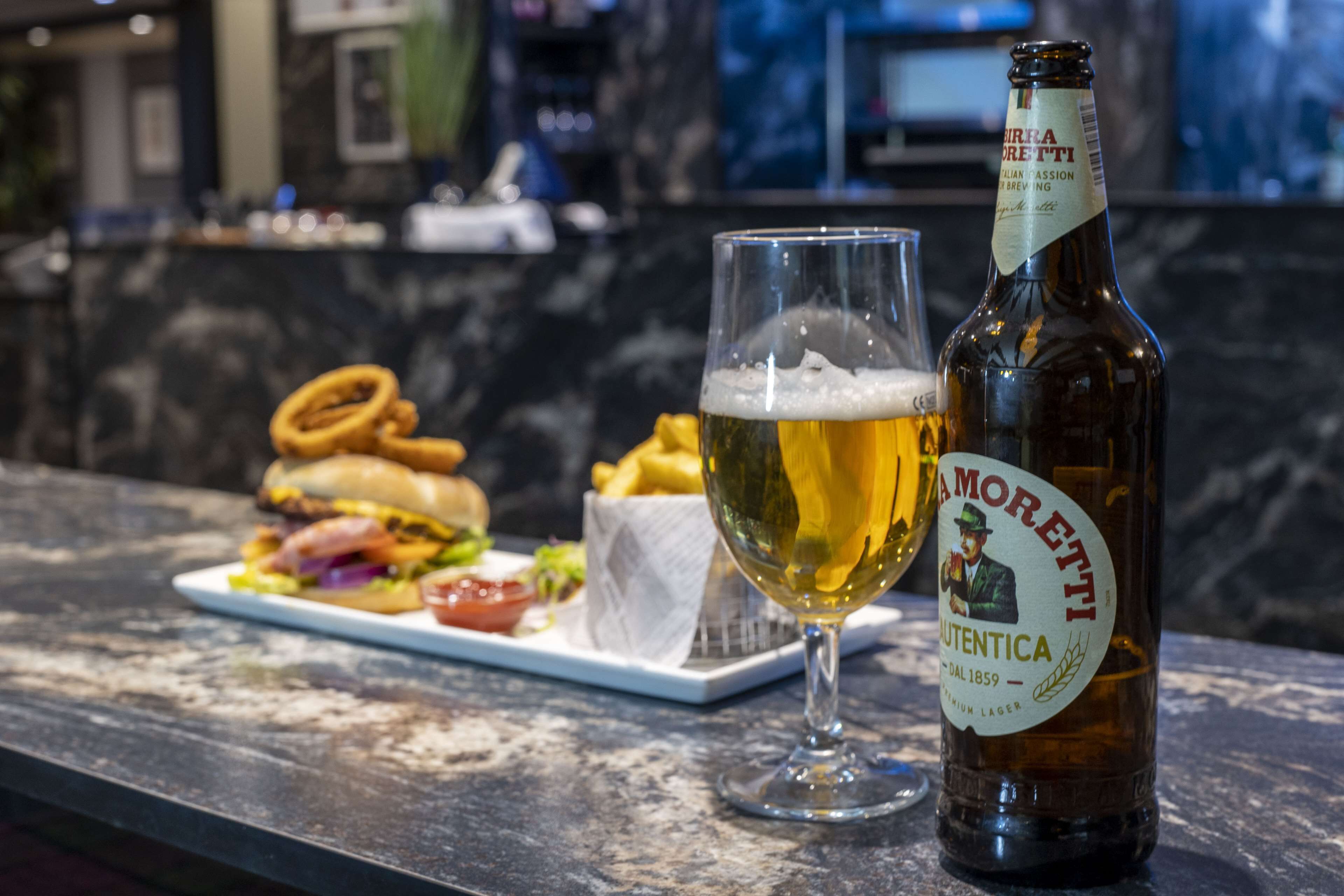 Une bouteille de bière et un verre sur une table, avec une assiette de nourriture.