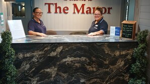 A reception desk with a marble top, two receptionists, a welcome sign, and a deposit sign. - Best Western Manor Hotel (Gravesend)