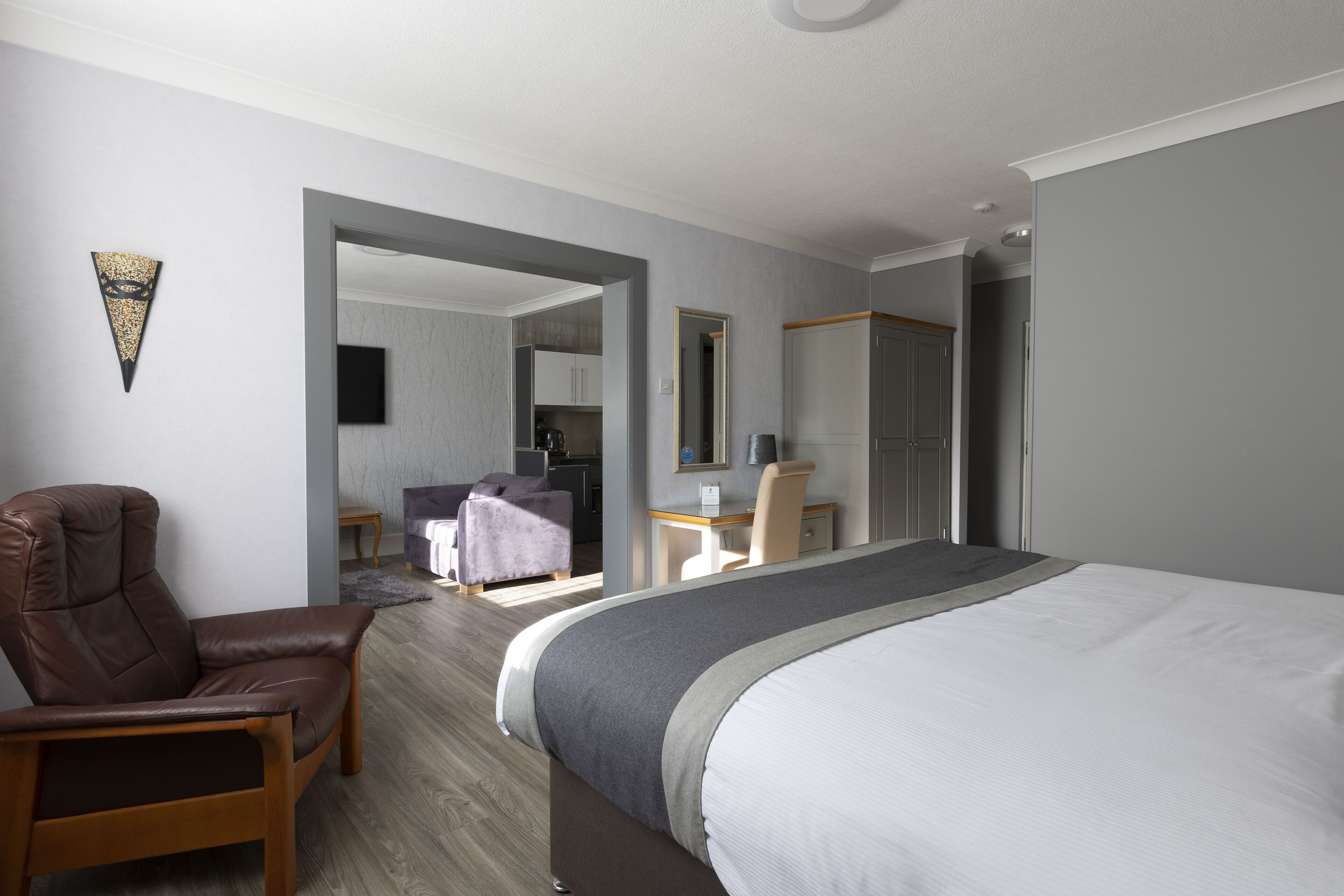 Quarto de hotel com uma cama grande, uma poltrona de couro, uma escrivaninha e um espelho.
