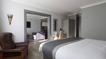 Quarto de hotel com uma cama grande, uma poltrona de couro, uma escrivaninha e um espelho.