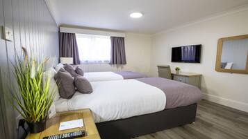 A hotel room with two beds, a TV, a mirror, and a plant.
